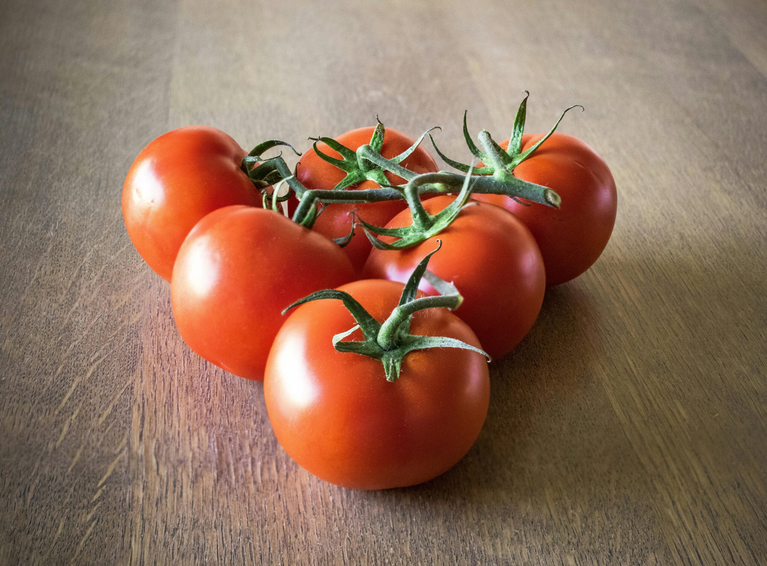 Ripe red tomatoes on a wooden table, showcasing their vibrant color and freshness.