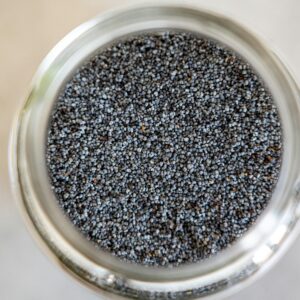 A detailed close-up of poppy seeds in a glass jar, highlighting texture and color.